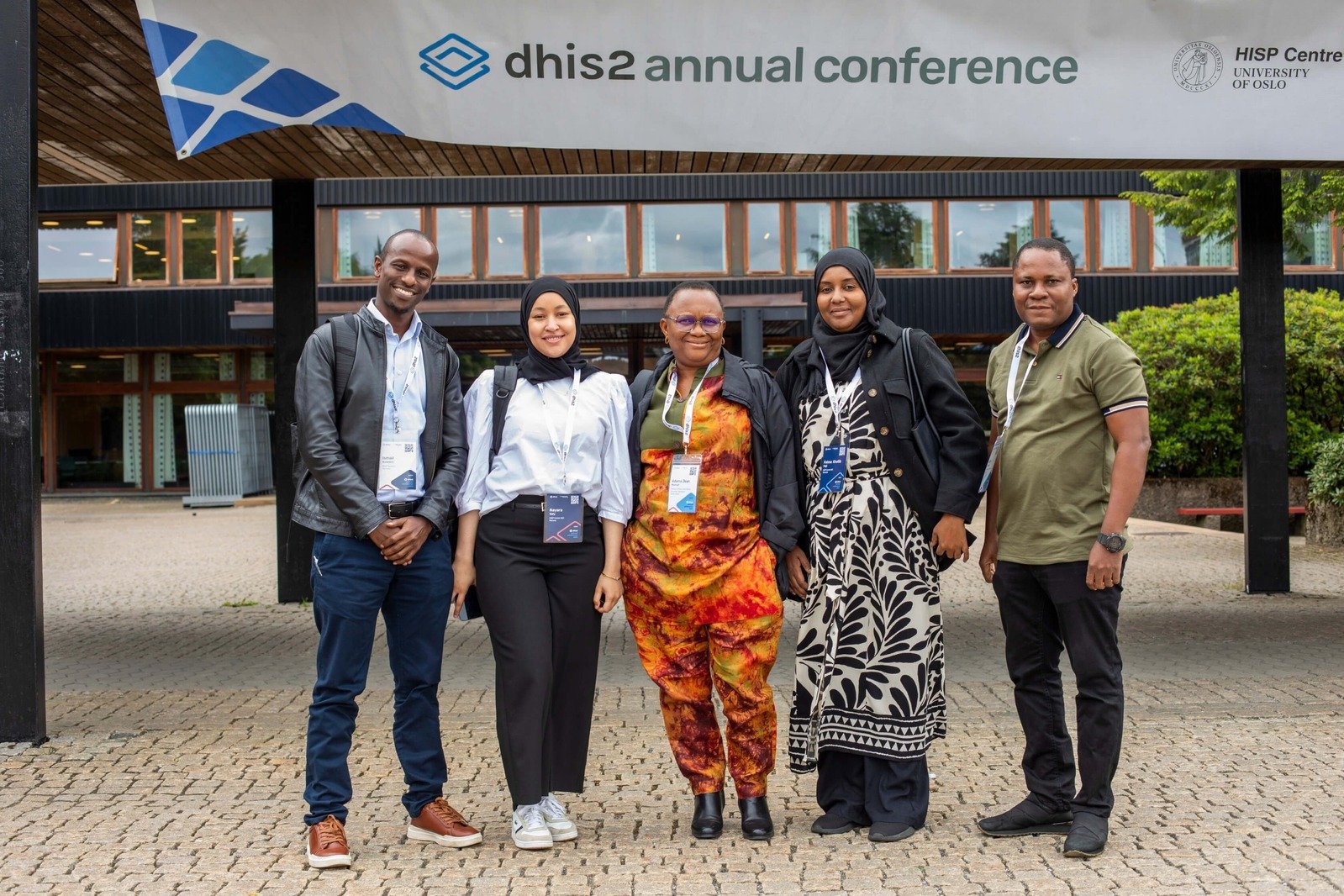 Five diverse DHIS2 Annual Conference attendees pose for a photo outside the HISP Centre at the University of Oslo.