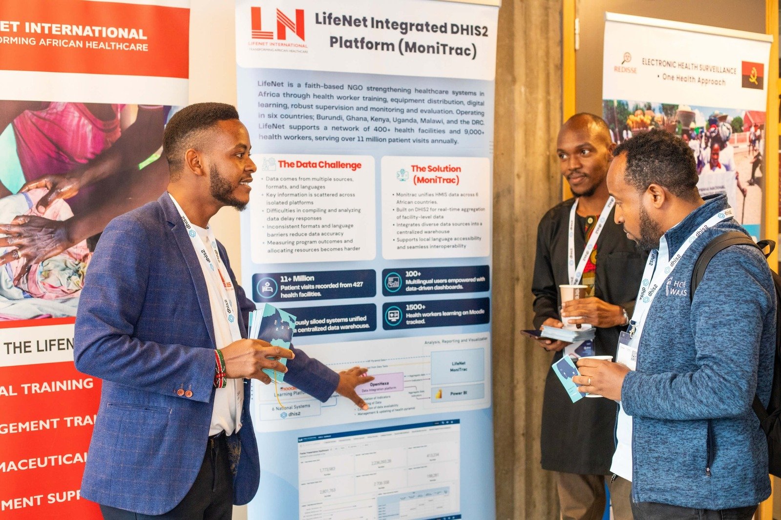 Three male attendees networking at the DHIS2 Annual Conference in front of a LifeNet International display.